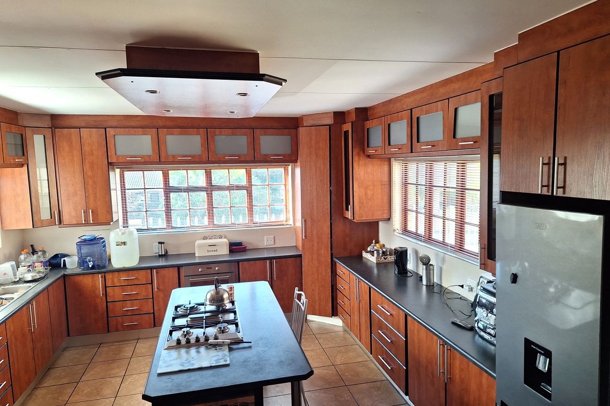 Spacious kitchen featuring extensive wood-finish cabinetry, a central island with a gas hob, dark countertops, and tiled flooring.