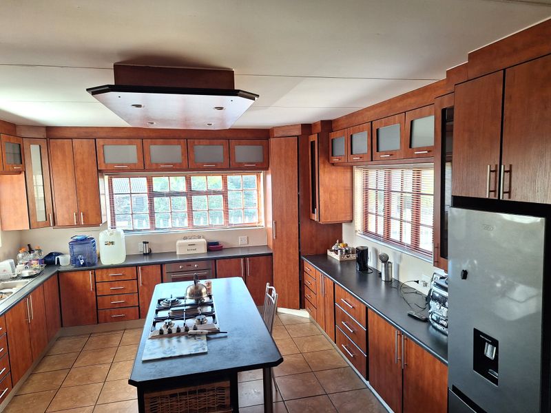 Spacious kitchen featuring extensive wood-finish cabinetry, a central island with a gas hob, dark countertops, and tiled flooring.
