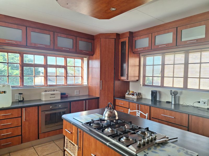 A well-maintained kitchen featuring wooden cabinetry, a central island with a gas hob, built-in oven, and ample natural light from large windows.