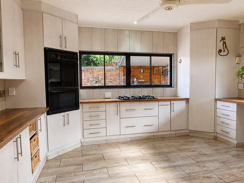A spacious kitchen featuring light-toned cabinetry, dark laminate countertops, a built-in oven, gas hob, and tiled flooring with a neutral backsplash.
