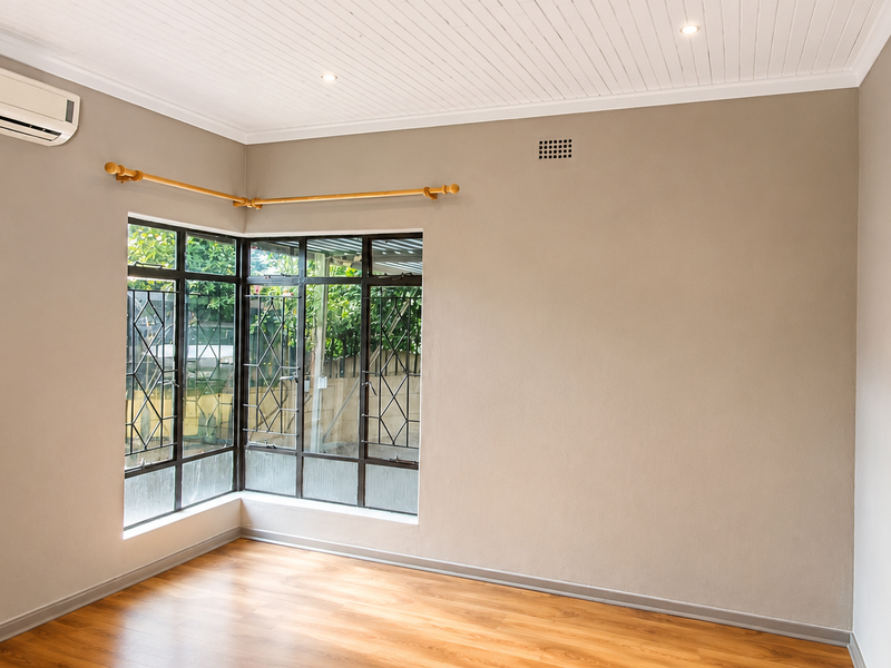 A bright, empty bedroom featuring laminate flooring, a split-system air conditioner, corner windows, and a unique recessed wall shelf.