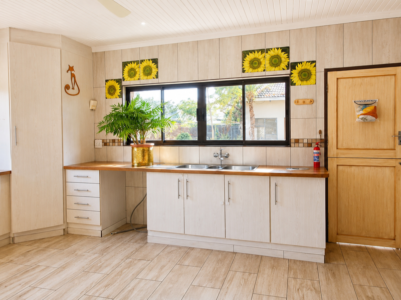 A functional kitchen featuring light-toned built-in cabinetry, wooden countertops, a double sink, and tiled finishes throughout, offering a clean and practical workspace.