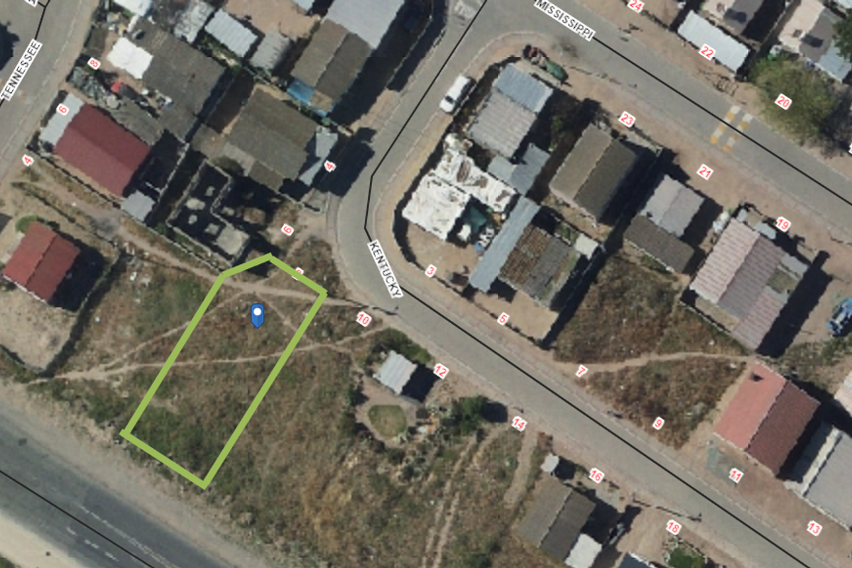 Aerial view of a vacant residential plot highlighted in green, situated within a developed neighborhood street layout.