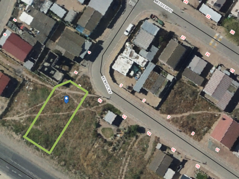 Aerial view of a vacant residential plot highlighted in green, situated within a developed neighborhood street layout.