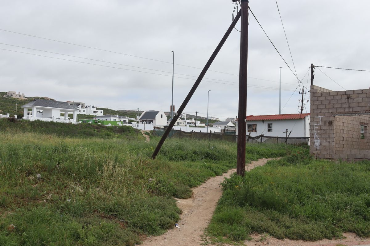 Vacant residential land featuring overgrown vegetation, an existing utility pole with overhead lines, and a partially constructed concrete block wall structure.