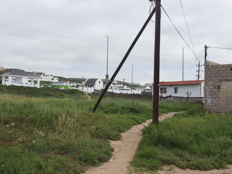 Vacant residential land featuring overgrown vegetation, an existing utility pole with overhead lines, and a partially constructed concrete block wall structure.