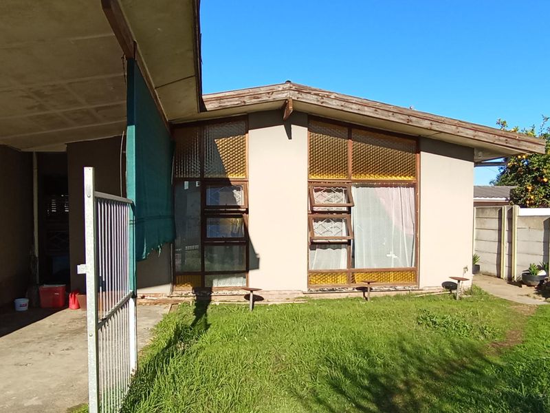 Rear exterior view of the property featuring a concrete patio area, large timber-framed windows with textured glass, and a precast concrete boundary wall.