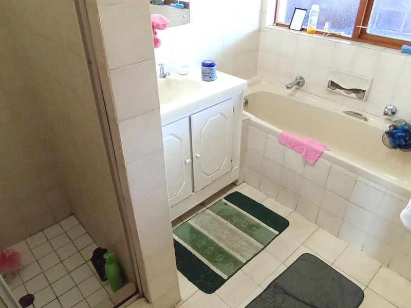 A functional bathroom featuring a built-in vanity, bathtub, and separate shower enclosure with dated tile finishes throughout.