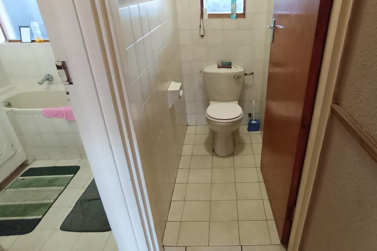 A functional bathroom featuring a standard toilet and bathtub with tiled wall and floor finishes, presenting a dated aesthetic.