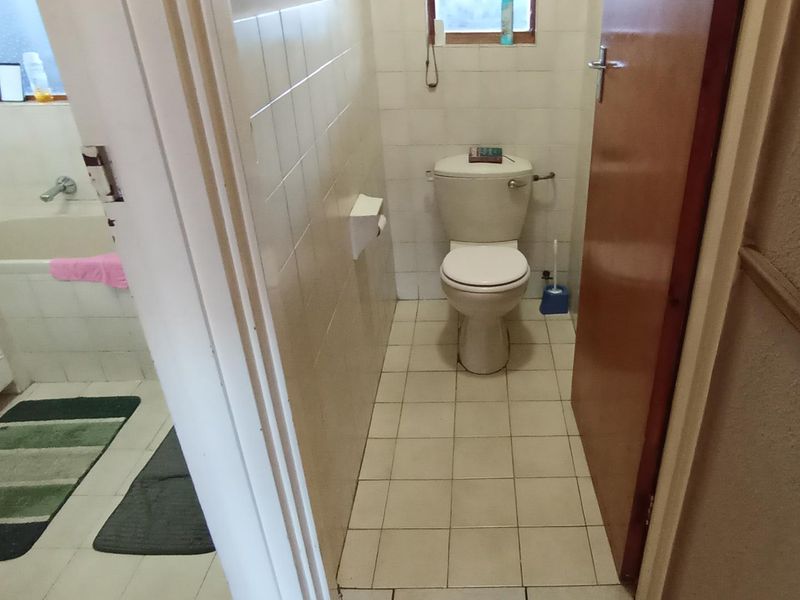 A functional bathroom featuring a standard toilet and bathtub with tiled wall and floor finishes, presenting a dated aesthetic.