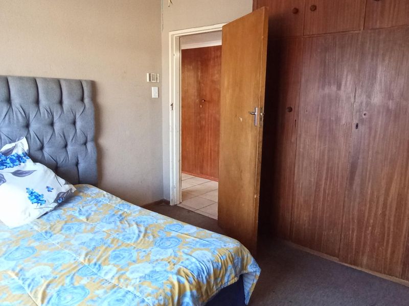 A bedroom featuring built-in wooden cupboards and carpeted flooring, offering a functional space with potential for modernization.