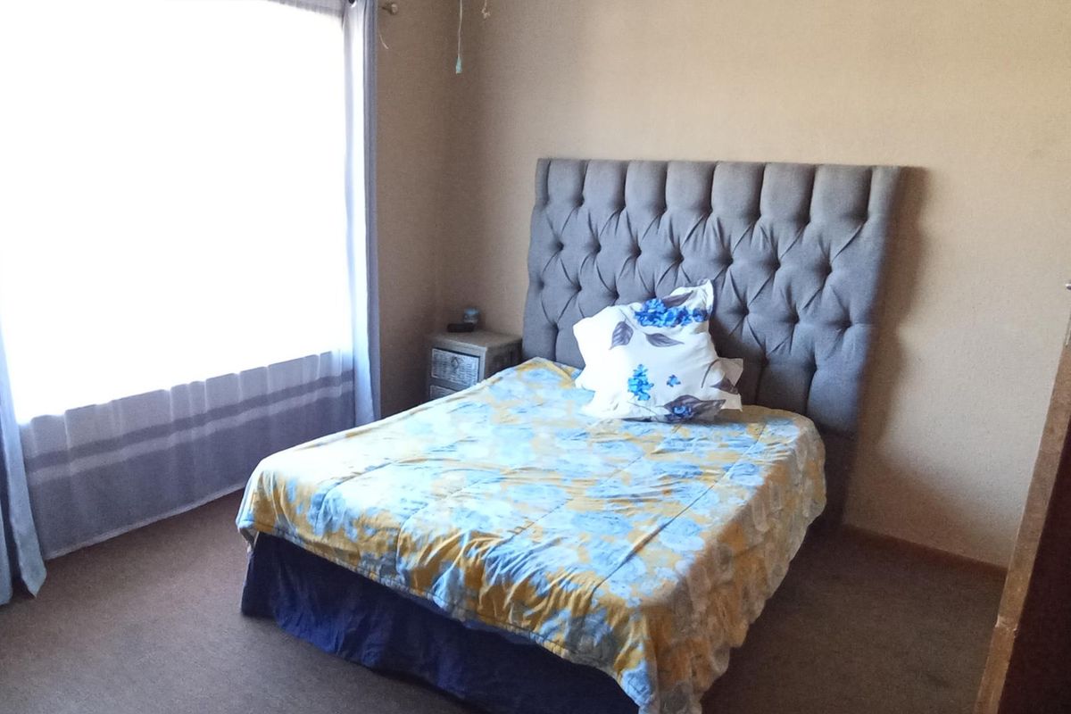 A standard bedroom featuring carpeted flooring and a large window allowing for natural light.