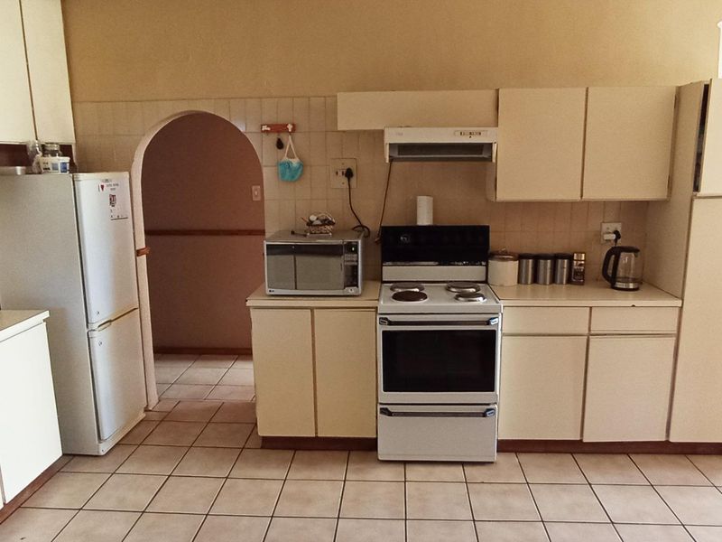 A functional kitchen featuring tiled flooring, a tiled backsplash, and built-in cabinetry with a freestanding stove and extractor fan.