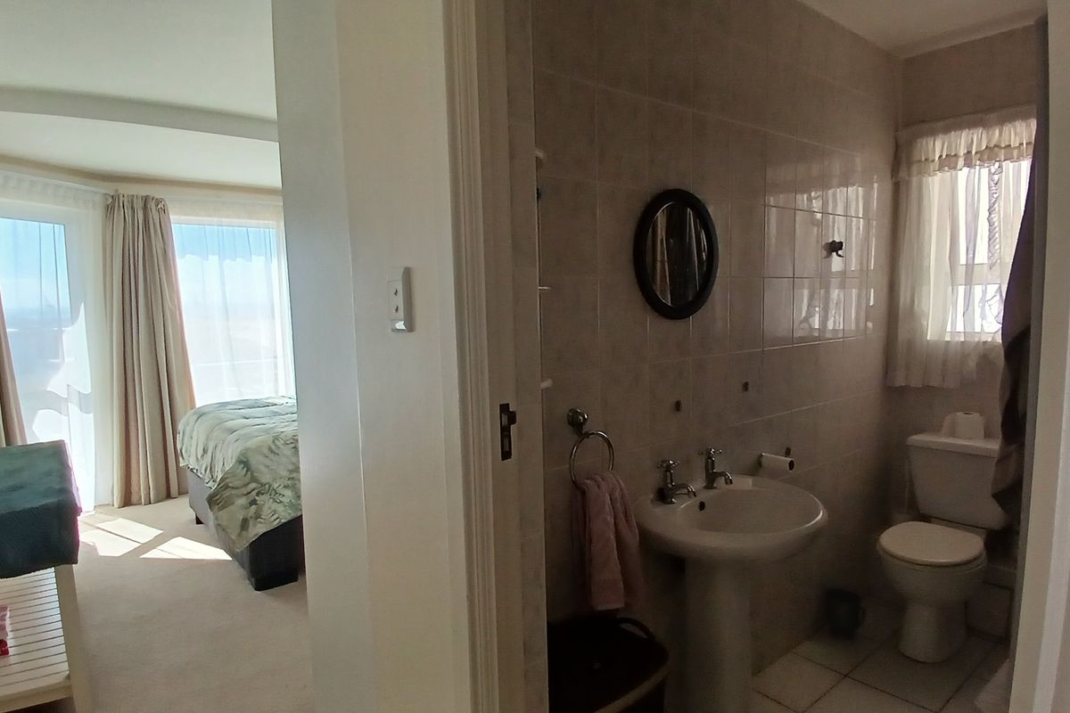 A functional bathroom featuring a pedestal basin and toilet, with neutral ceramic wall and floor tiling, adjacent to a bedroom area.