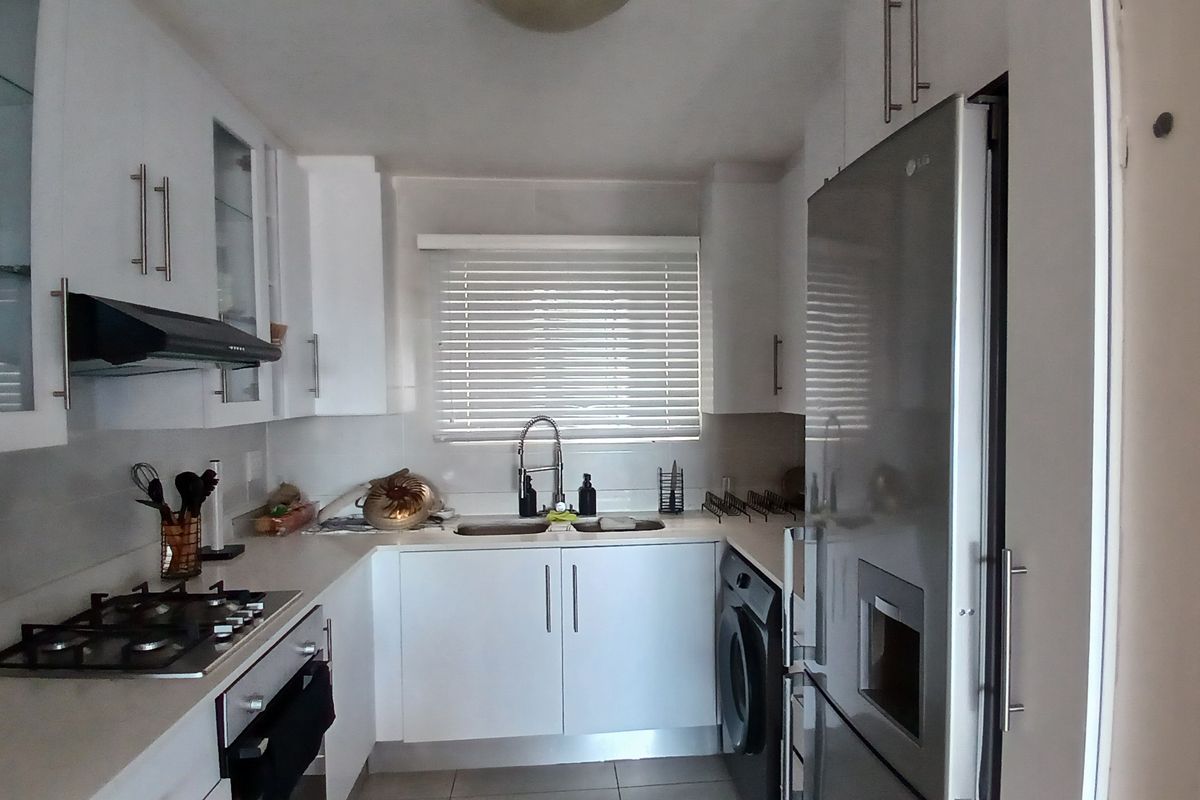 A modern, compact kitchen featuring white cabinetry, a gas hob, extractor fan, built-in oven, and a double sink with a mixer tap.