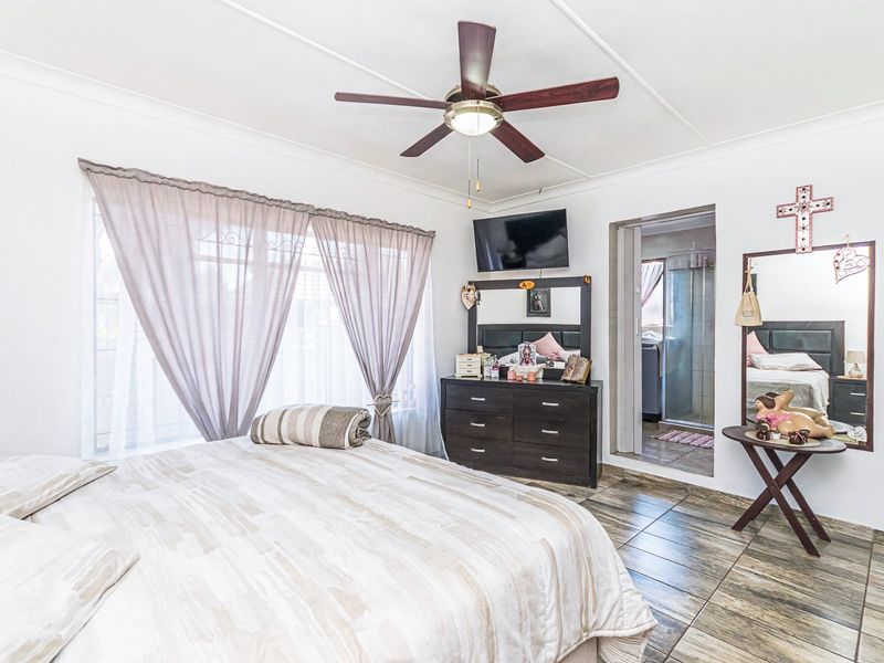 A spacious bedroom featuring tiled flooring, a ceiling fan, and direct access to an en-suite bathroom.