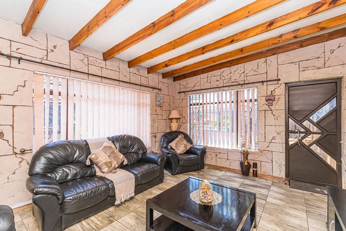 Living room featuring exposed timber ceiling beams, tiled flooring, and distinctive textured wall finishes with large windows and vertical blinds.