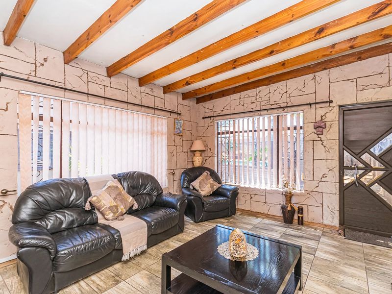 Living room featuring exposed timber ceiling beams, tiled flooring, and distinctive textured wall finishes with large windows and vertical blinds.