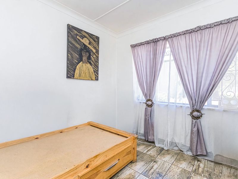A bedroom featuring tiled flooring and a window fitted with security bars, offering a functional space with neutral finishes.