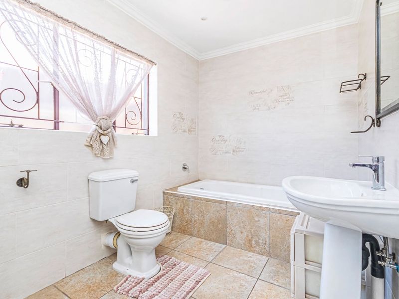 A functional bathroom featuring a pedestal basin, built-in bathtub, and tiled finishes throughout, complemented by natural light from the window.