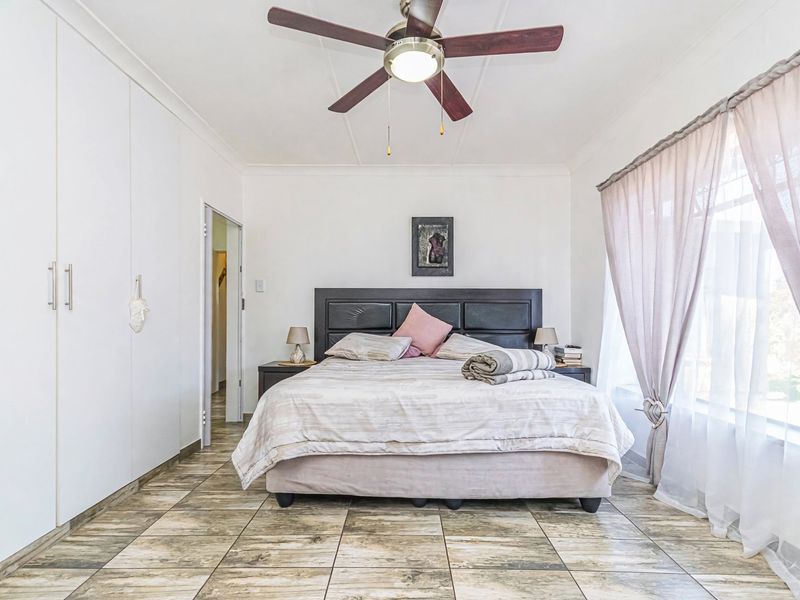 A well-maintained bedroom featuring tiled flooring, built-in cupboards, and a ceiling fan, offering a clean and functional living space.