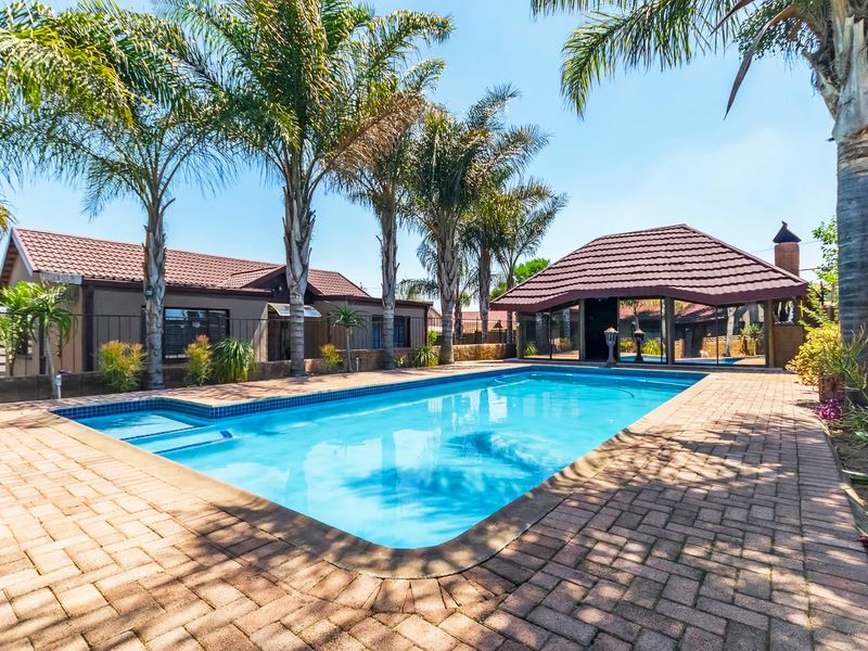 Outdoor pool area featuring a paved deck, swimming pool, and a covered thatched lapa structure, ideal for entertainment.