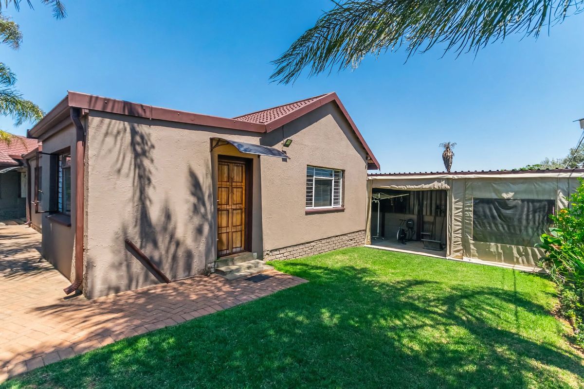 Rear view of the property featuring a paved patio area, a lawn, and an attached metal carport structure.