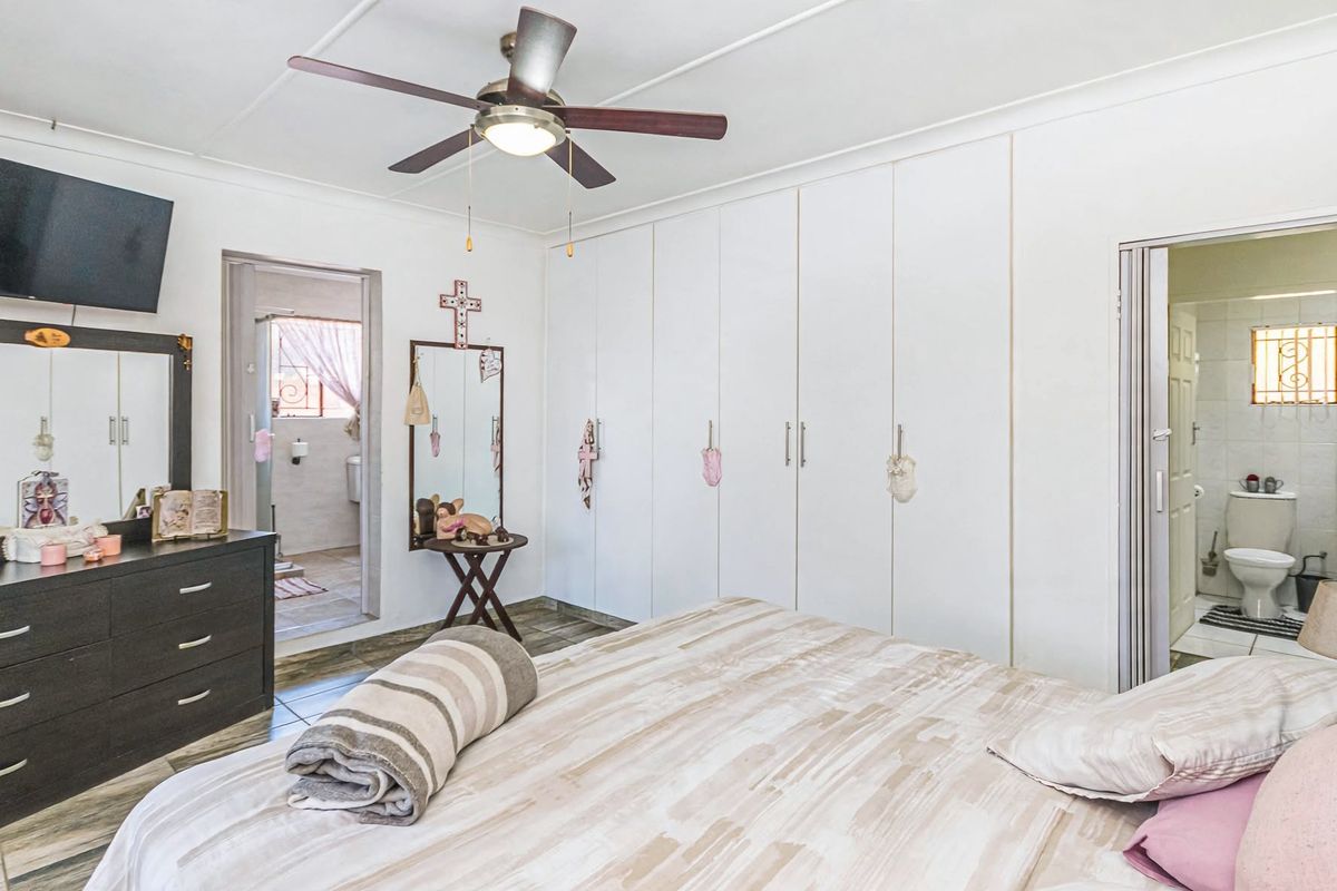 Spacious bedroom featuring built-in cupboards, tiled flooring, a ceiling fan, and direct access to an en-suite bathroom.