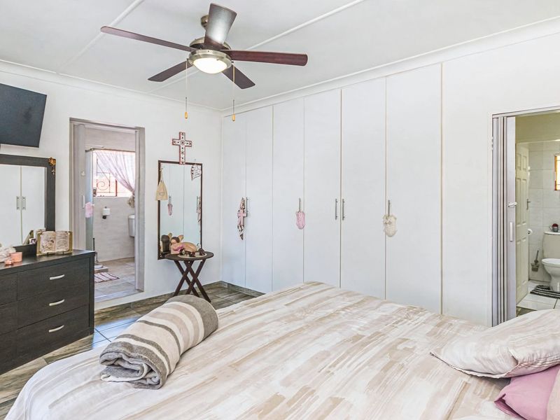 Spacious bedroom featuring built-in cupboards, tiled flooring, a ceiling fan, and direct access to an en-suite bathroom.