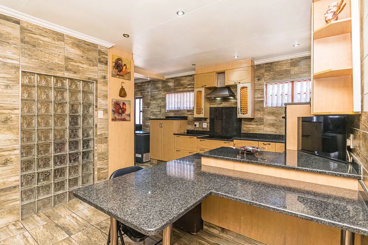 A spacious kitchen featuring granite countertops, extensive built-in cabinetry, a unique glass block wall feature, and modern recessed lighting.