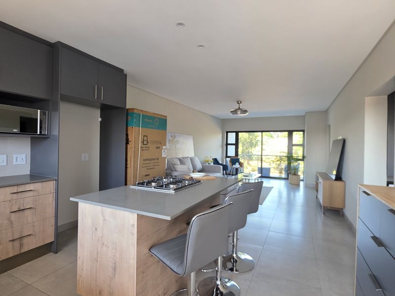 Modern open-plan living area featuring a contemporary kitchen with a central island, gas hob, and seamless flow to the balcony through sliding glass doors.