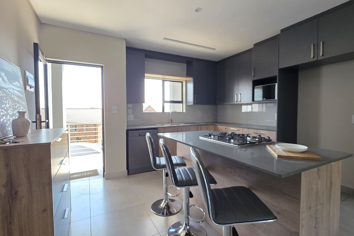 Modern kitchen featuring dark cabinetry, stone countertops, a central island with a gas hob, and direct access to an outdoor balcony area.