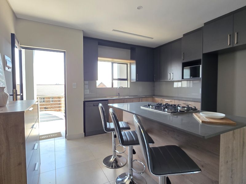 Modern kitchen featuring dark cabinetry, stone countertops, a central island with a gas hob, and direct access to an outdoor balcony area.