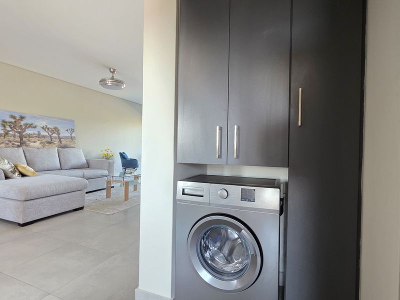 A compact laundry nook featuring built-in dark cabinetry and an integrated washing machine, conveniently located adjacent to the open-plan living area.