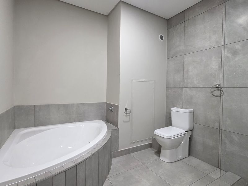 Modern bathroom featuring a corner bathtub, a separate shower area with a glass screen, and contemporary grey tiling throughout.