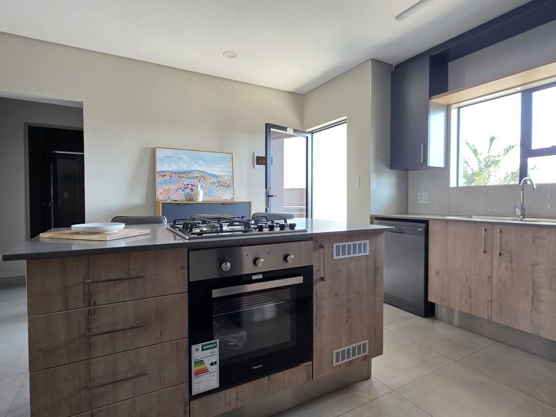 Modern kitchen featuring a central island with built-in oven and gas hob, stone countertops, and ample cabinetry, with an adjacent laundry area.