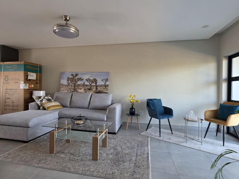 Modern open-plan living area featuring neutral tiled flooring, a ceiling fan, and seamless access to an outdoor space through large sliding glass doors.