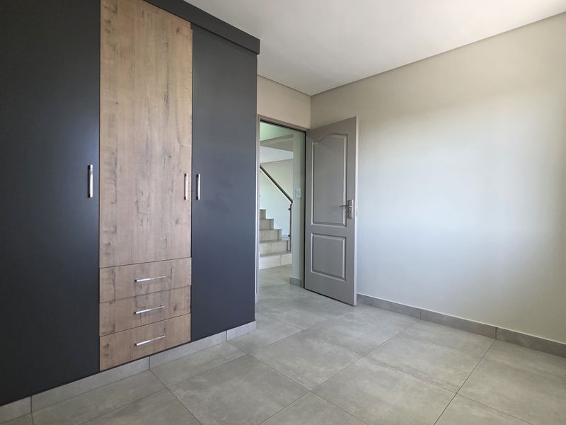 A clean, modern bedroom featuring neutral tiled flooring and a contemporary built-in wardrobe with a two-tone finish.