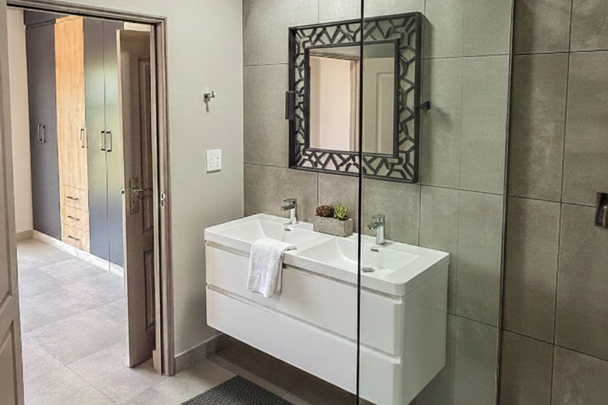 Modern bathroom featuring a sleek double vanity, large format wall tiles, and a frameless glass shower screen, with adjacent built-in storage.