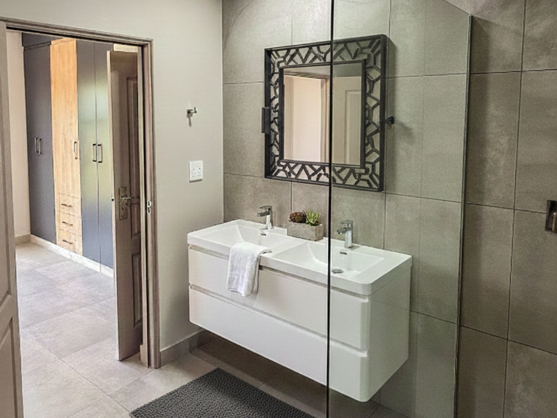 Modern bathroom featuring a sleek double vanity, large format wall tiles, and a frameless glass shower screen, with adjacent built-in storage.