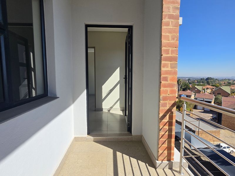 A clean, modern balcony featuring tiled flooring, a stainless steel balustrade, and an exposed brick pillar, offering elevated views of the surrounding neighbourhood.