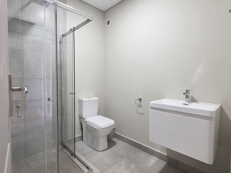 A modern, clean bathroom featuring a glass-enclosed shower, wall-mounted vanity, and neutral tiled finishes throughout.