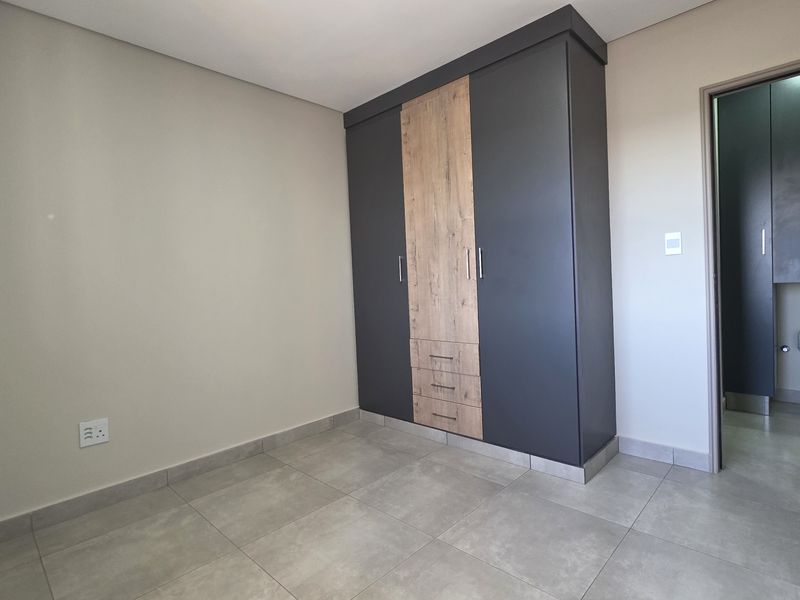 A clean, empty bedroom featuring modern built-in wardrobes with a two-tone finish and neutral tiled flooring.