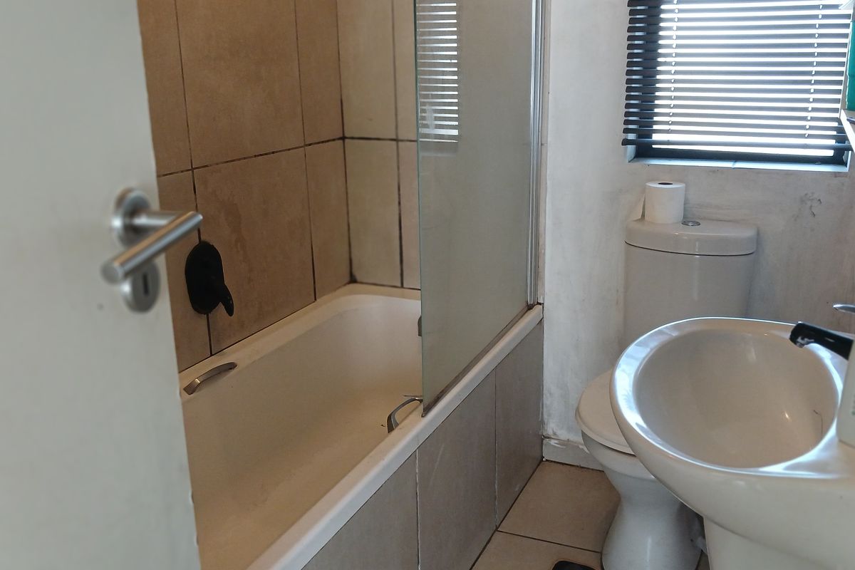 A functional bathroom featuring a bathtub with a glass screen, pedestal basin, and toilet, finished with neutral wall and floor tiling.