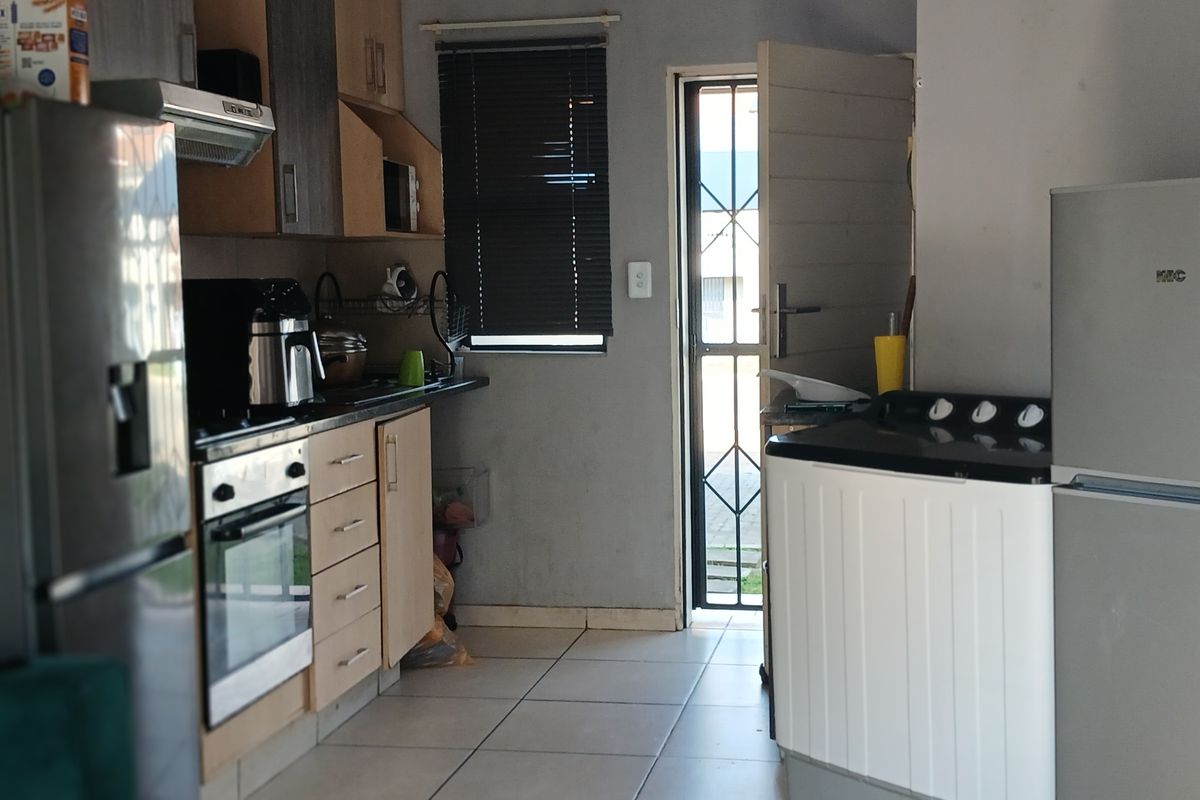 A functional kitchen featuring built-in cabinetry, an integrated oven and hob, tiled flooring, and direct access to an exterior security gate.