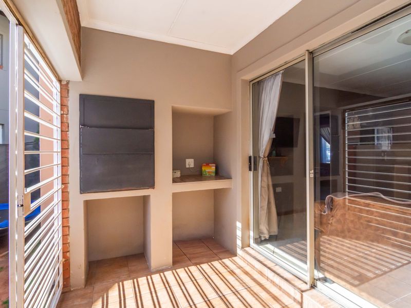 Covered patio area featuring a built-in braai, tiled flooring, and sliding glass door access to the interior living space.