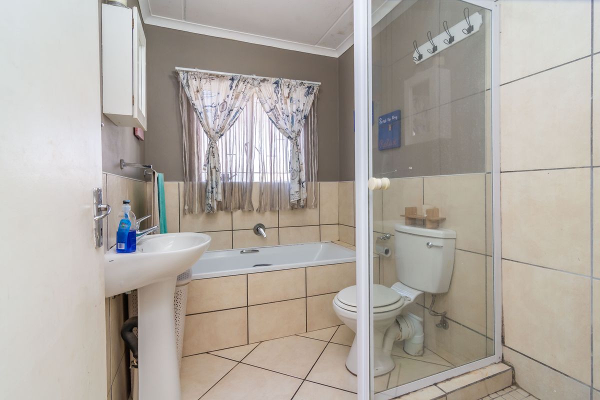 A functional bathroom featuring a pedestal basin, built-in bathtub, toilet, and a separate glass-enclosed shower area with neutral ceramic tiling.