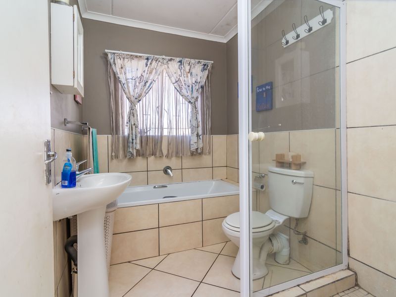 A functional bathroom featuring a pedestal basin, built-in bathtub, toilet, and a separate glass-enclosed shower area with neutral ceramic tiling.