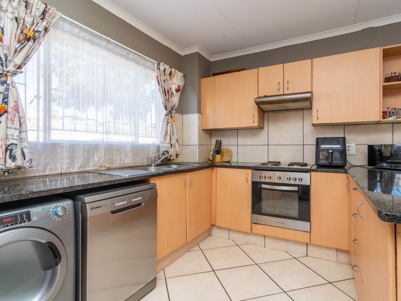 Functional kitchen featuring light wood cabinetry, granite countertops, stainless steel oven and hob, and tiled flooring with integrated laundry appliance space.