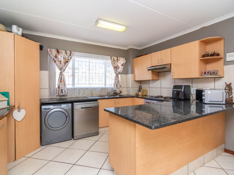 A functional kitchen featuring laminate cabinetry, granite countertops, tiled backsplash, and integrated space for laundry appliances.